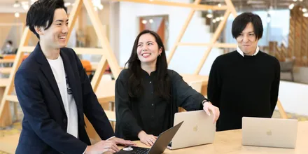 Three people standing at a table, laptops open
